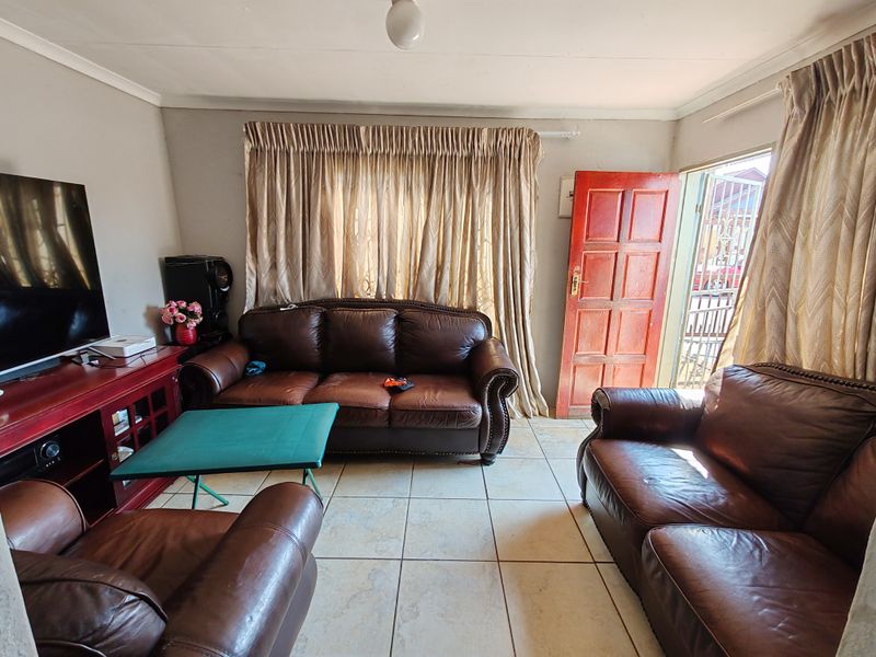 A functional living room featuring tiled flooring, a solid wood entrance door with security gate, and neutral wall finishes.