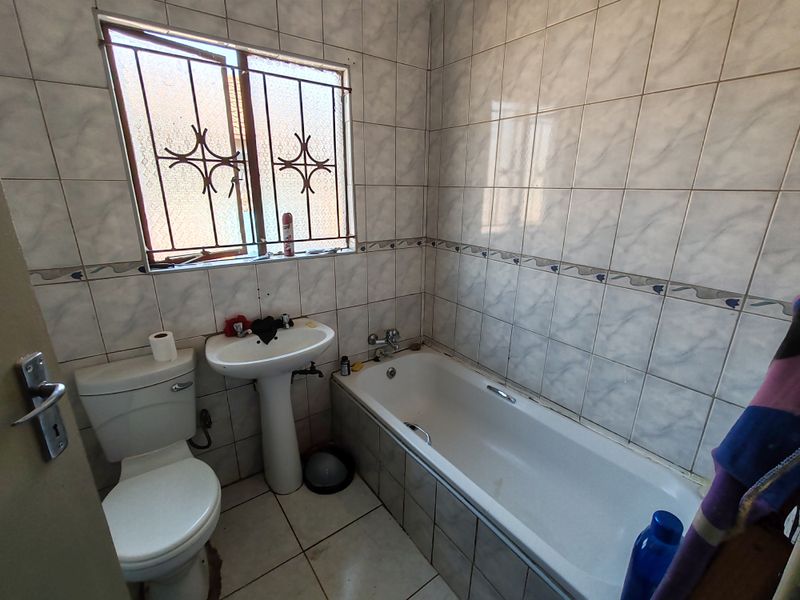 A functional bathroom featuring a pedestal basin, bathtub, and toilet with full-height wall tiling and security bars on the window.