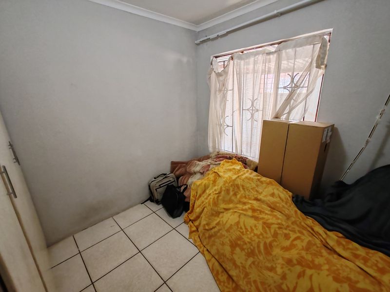 A bedroom featuring tiled flooring, a built-in cupboard, and a window fitted with a security gate.