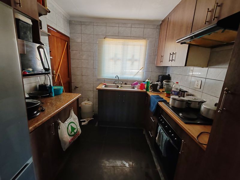 A functional kitchen featuring built-in wooden cabinetry, a double sink, and integrated cooking appliances with tiled splashbacks.
