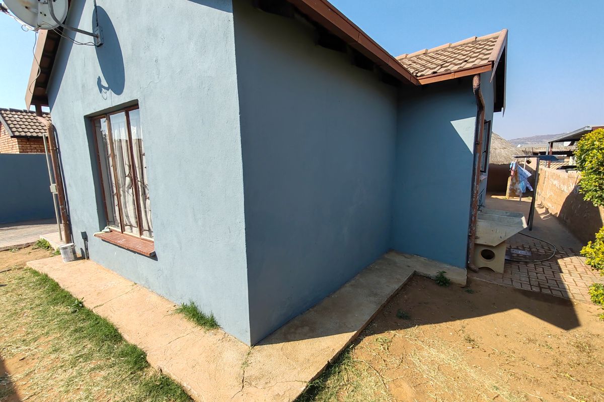Rear exterior view of the house featuring a blue painted facade, tiled roof, and a concrete apron with an external wash basin.