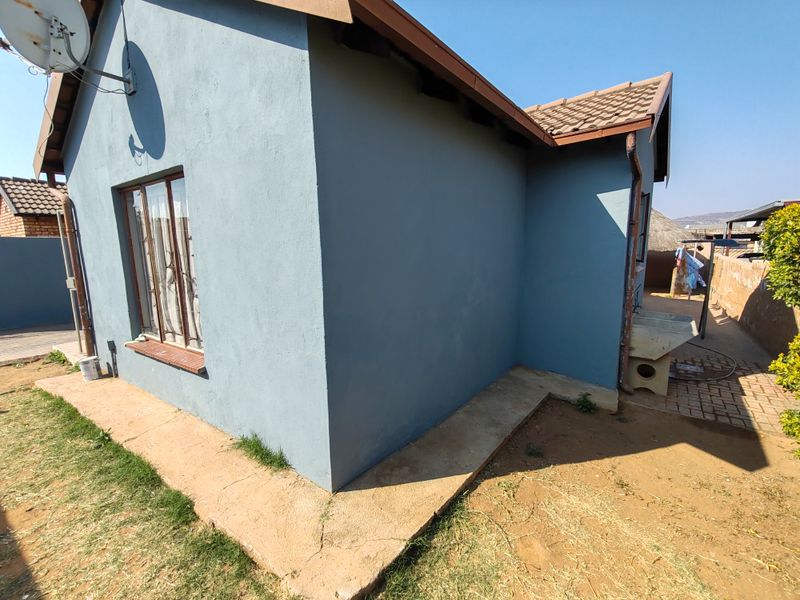 Rear exterior view of the house featuring a blue painted facade, tiled roof, and a concrete apron with an external wash basin.