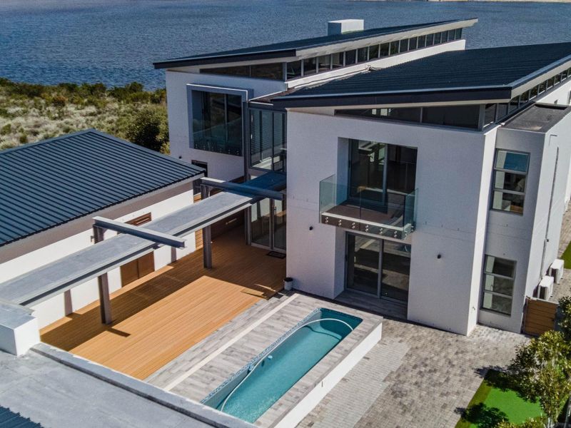 Aerial view of a modern multi-level residence featuring a swimming pool, timber deck, and contemporary architectural design overlooking the water.