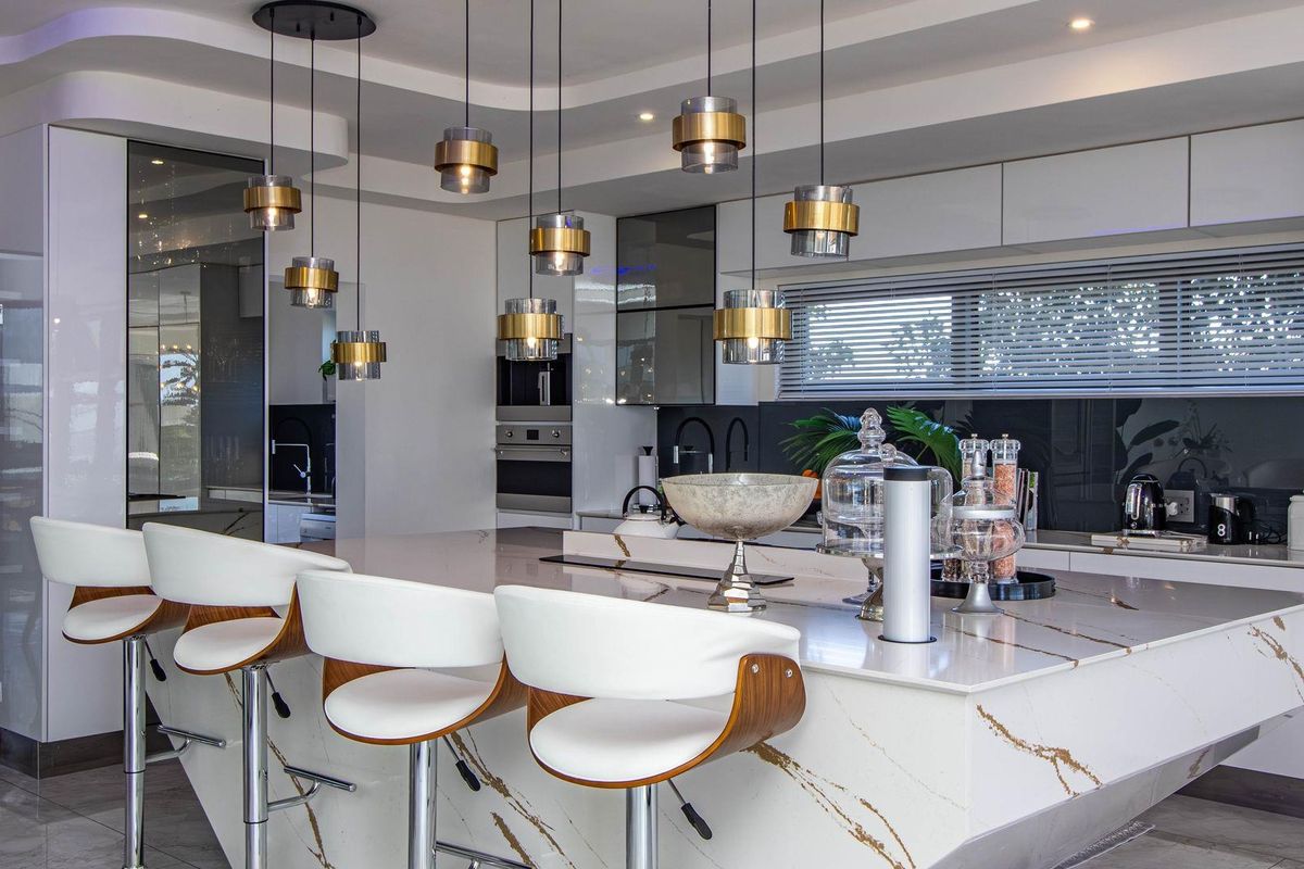 Modern kitchen featuring a large stone island, high-gloss cabinetry, built-in appliances, and elegant pendant lighting in a contemporary open-plan setting.