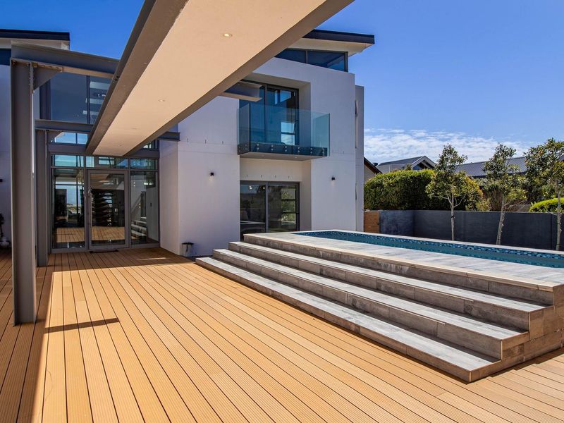 Modern outdoor entertainment area featuring a raised swimming pool, composite decking, and a sleek architectural steel structure with glass balcony access.