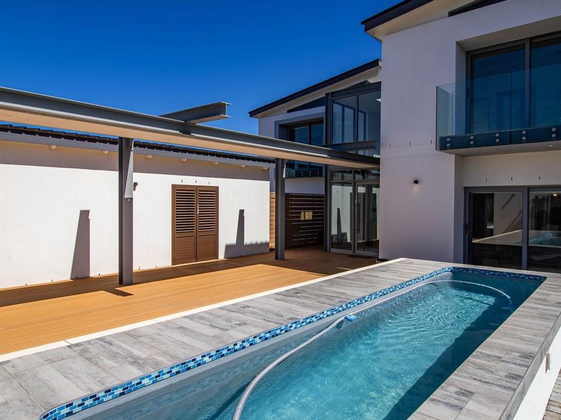 Modern outdoor area featuring a swimming pool with tiled surround, timber decking, and a steel pergola, adjacent to the main house structure.