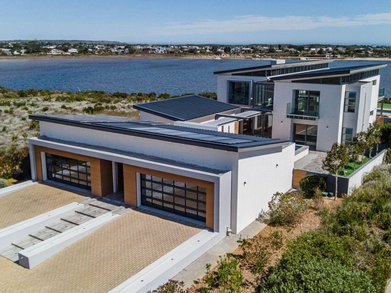 Aerial view of a modern multi-level residence featuring a double garage, solar panels, and scenic waterfront positioning.