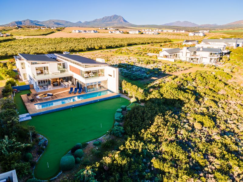 Aerial view of a modern luxury residence featuring a swimming pool, timber deck, private putting green, and scenic mountain views.