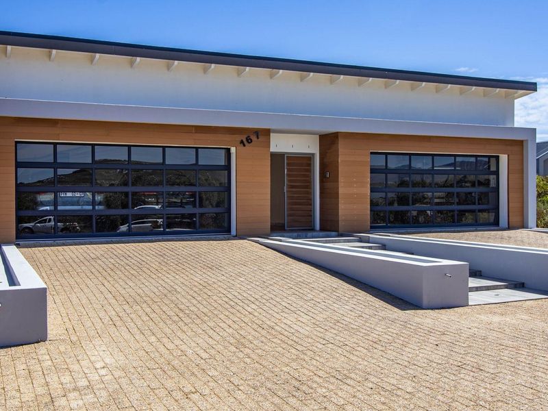 Modern single-story residence featuring a double garage, timber-clad facade, and a clean, paved driveway with integrated concrete landscaping elements.