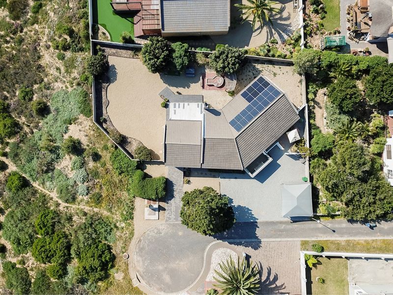 Aerial view of the property showcasing the roof structure, solar panel installation, paved driveway, and surrounding landscaped garden area.