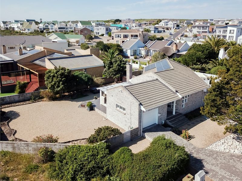 Aerial view of a residential property featuring a brick exterior, tiled roof with solar panels, a garage, and a paved driveway in a coastal neighborhood.