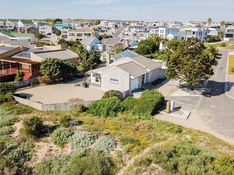 Aerial view of a residential property featuring a brick exterior, tiled roof with solar panels, paved driveway, and established garden in a coastal neighborhood.