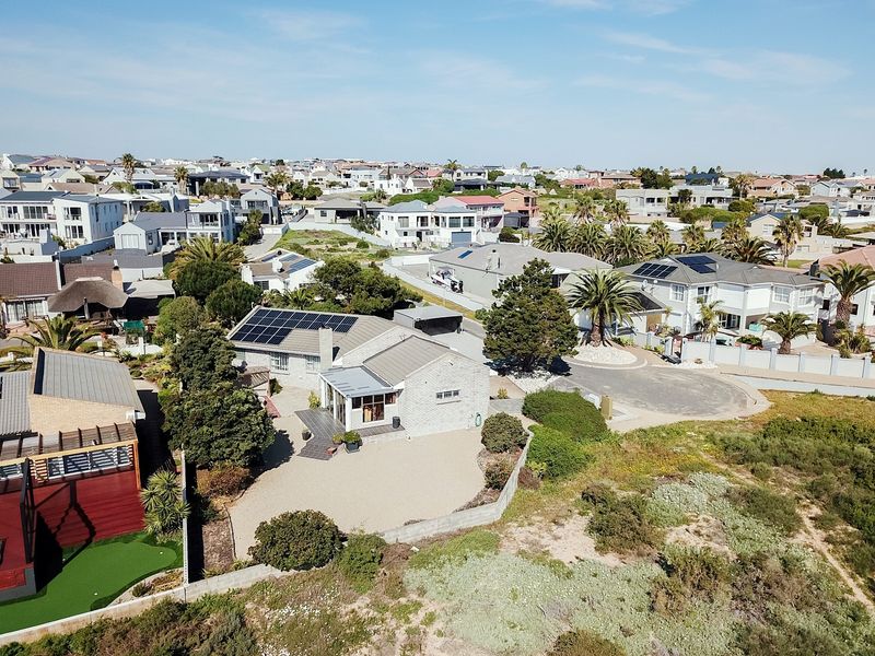 Aerial view of a residential property featuring a tiled roof with solar panels, a paved driveway, and established garden surroundings in a coastal neighborhood.