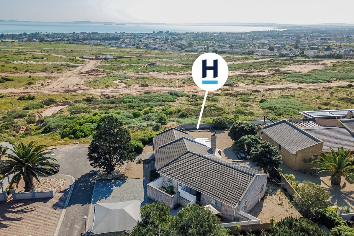 Aerial view of a residential property featuring a tiled roof, brick chimney, and surrounding landscaped grounds with coastal views in the distance.