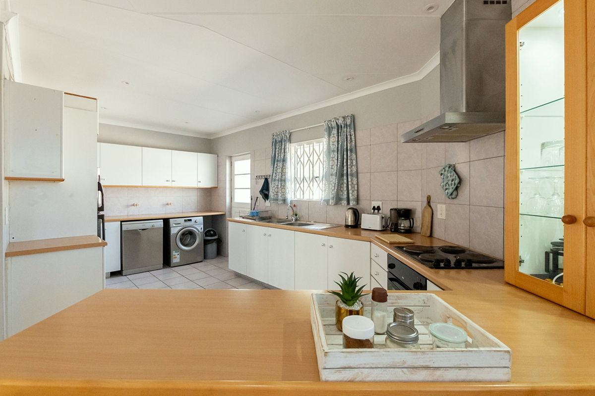 Functional kitchen featuring white cabinetry, laminate countertops, tiled backsplash, built-in oven, hob, extractor fan, and dedicated space for laundry appliances.