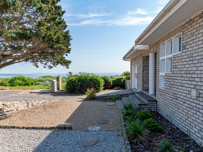 A well-maintained brick exterior facade featuring a paved walkway, landscaped garden beds, and a clear view of the surrounding landscape.