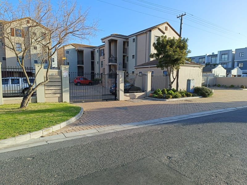 Front exterior view of a secure apartment complex featuring a paved driveway, metal security gate, electric fencing, and integrated post boxes.