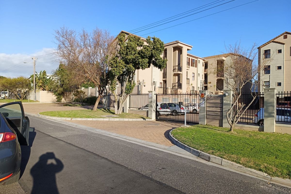 Front exterior view of the apartment complex featuring a secure gated entrance, paved driveway, and perimeter electric fencing.