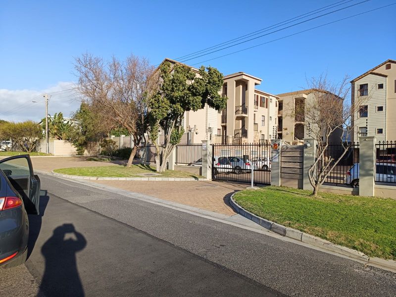 Front exterior view of the apartment complex featuring a secure gated entrance, paved driveway, and perimeter electric fencing.