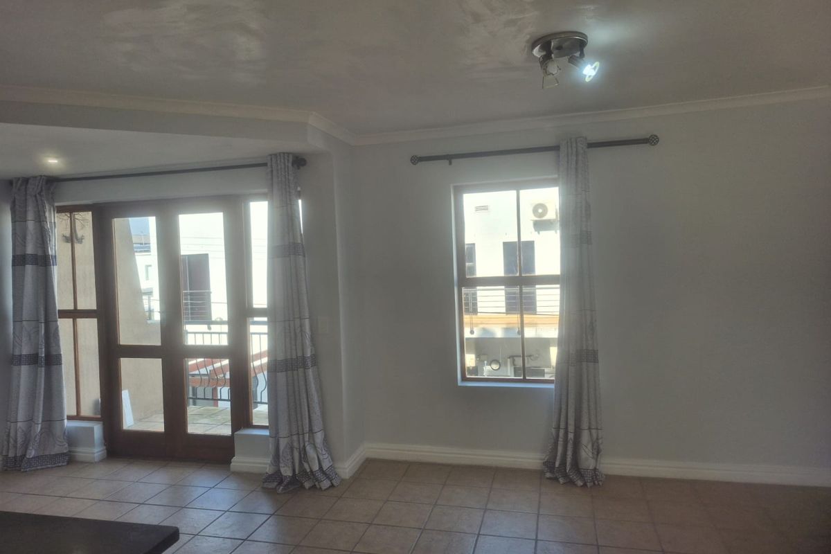 An empty living room featuring tiled flooring, ceiling coving, and access to a balcony through a wooden framed glass door.