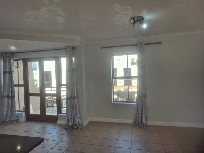 An empty living room featuring tiled flooring, ceiling coving, and access to a balcony through a wooden framed glass door.