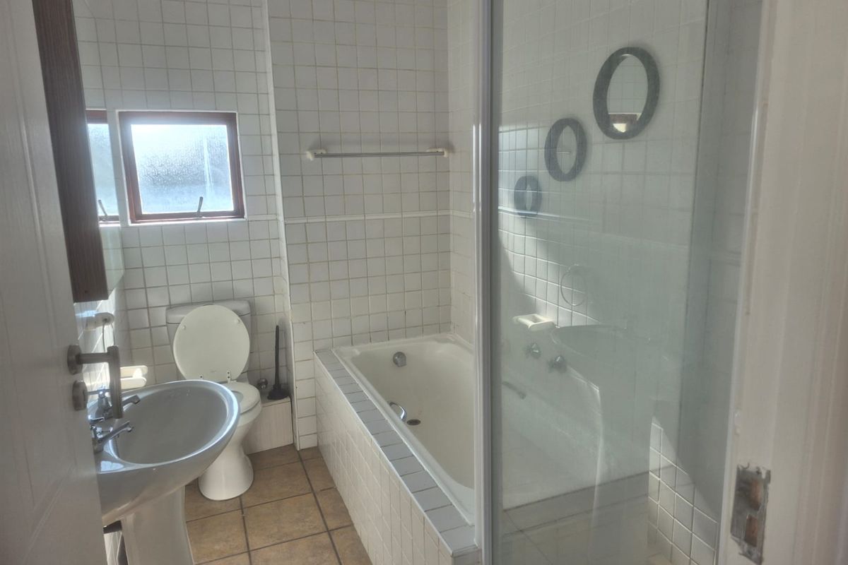 A functional bathroom featuring a pedestal basin, toilet, built-in bathtub, and a separate shower enclosure with tiled finishes throughout.