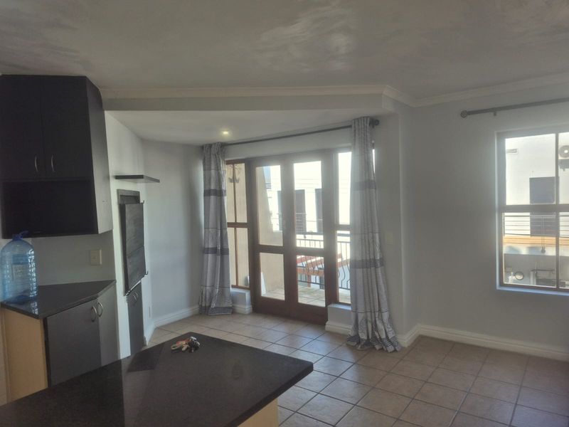 Open plan living area featuring tiled flooring, dark cabinetry with granite countertops, and direct access to a balcony through sliding glass doors.