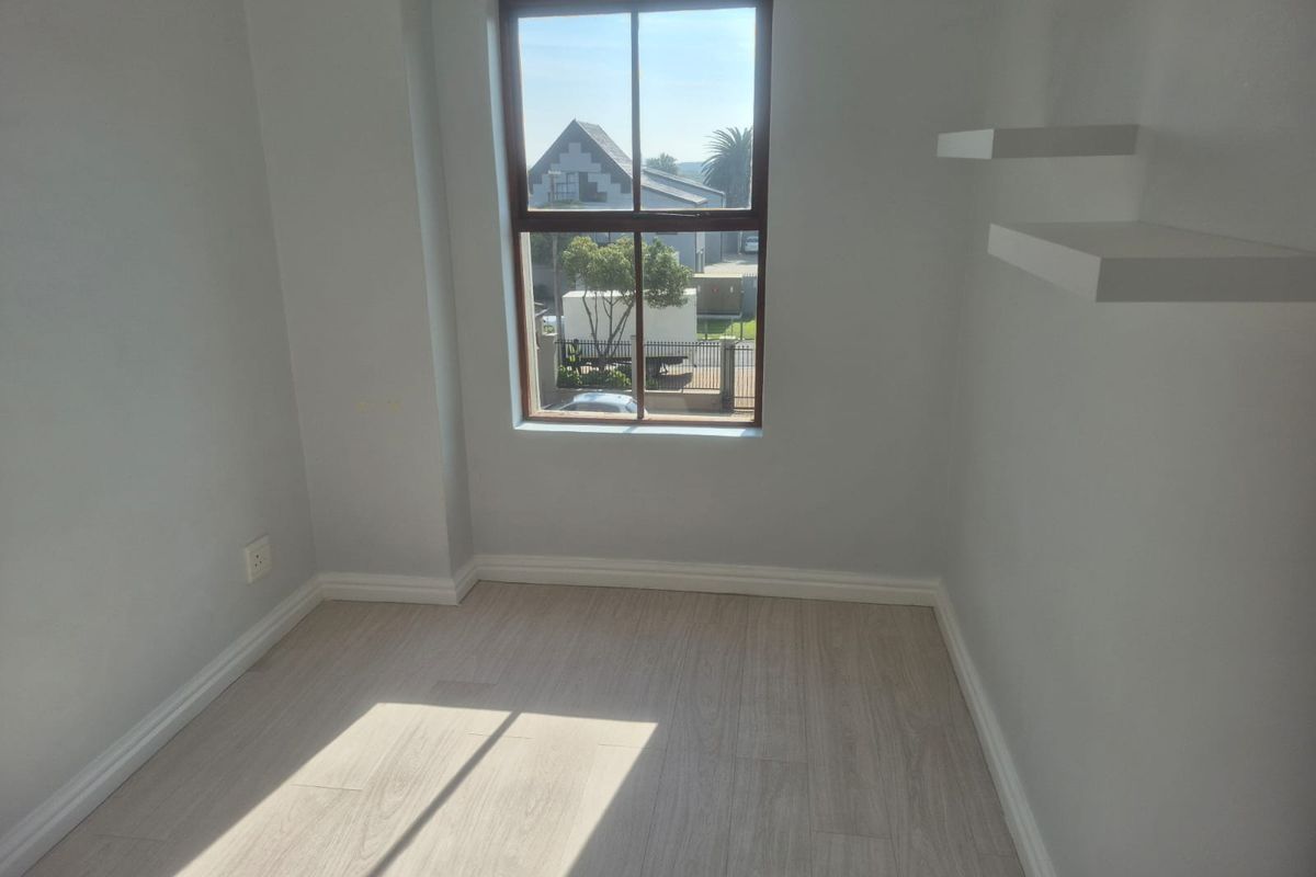 A bright, empty bedroom featuring light-toned laminate flooring, neutral walls, and built-in floating shelves, offering a clean and versatile space.