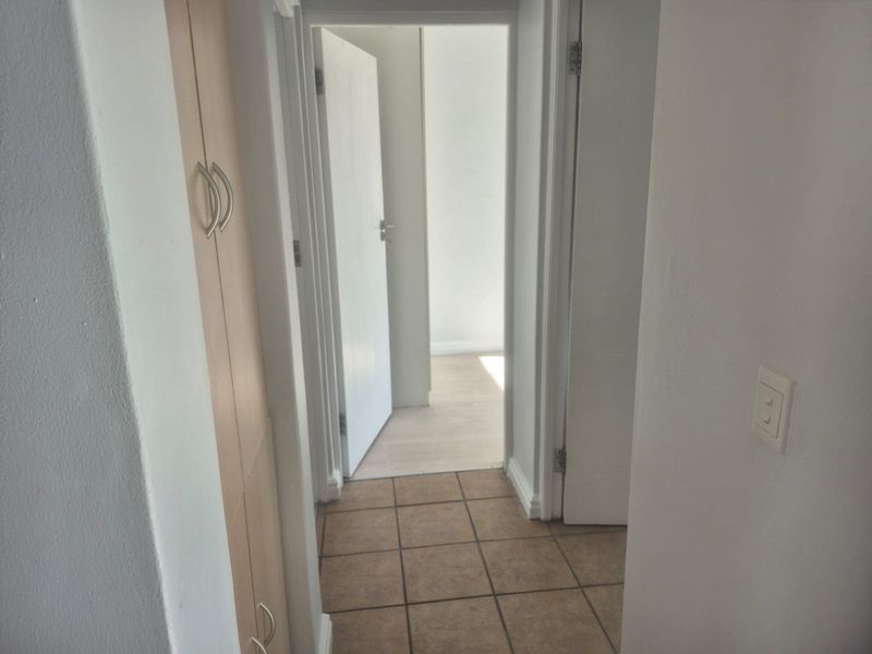 A functional hallway featuring tiled flooring and a built-in storage cupboard, providing access to adjacent rooms within the apartment.