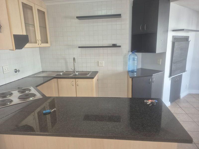A functional kitchen featuring granite countertops, built-in cabinetry, an electric hob, and a double sink with a tiled backsplash.