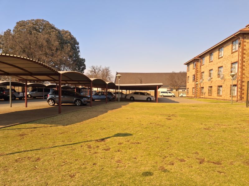 Exterior view of the apartment complex featuring a large lawn area and covered parking bays for residents.