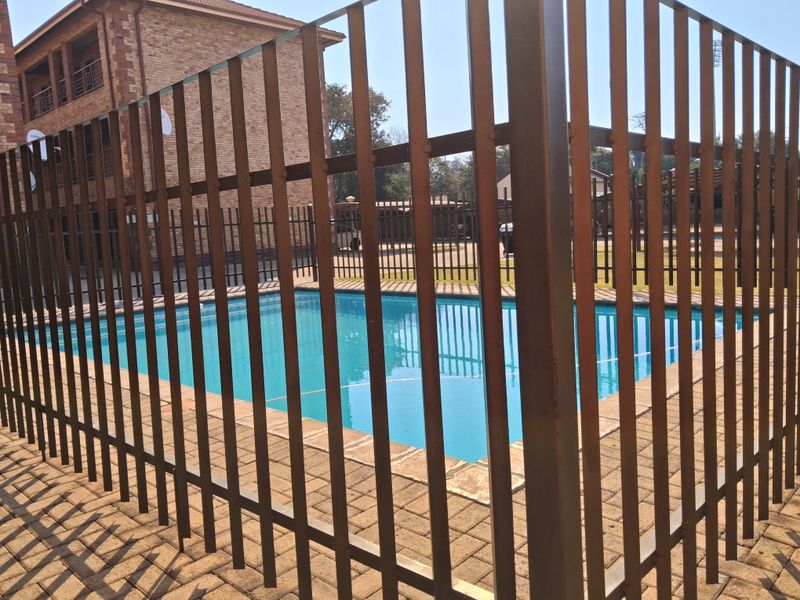 A communal swimming pool area featuring paved surrounds and secure metal perimeter fencing within an apartment complex.