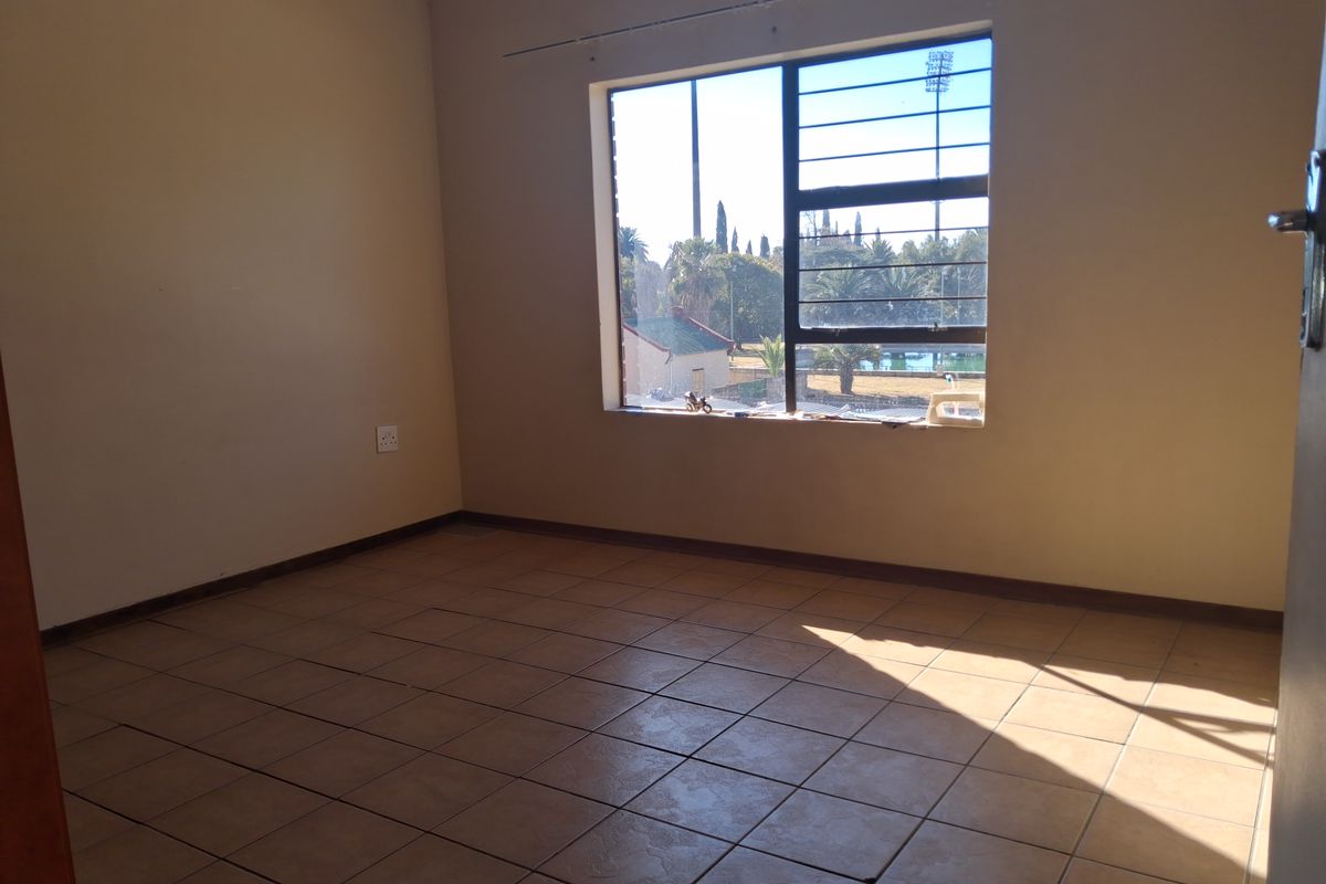 An empty bedroom featuring tiled flooring and a window with security bars, offering a view of the surrounding area.