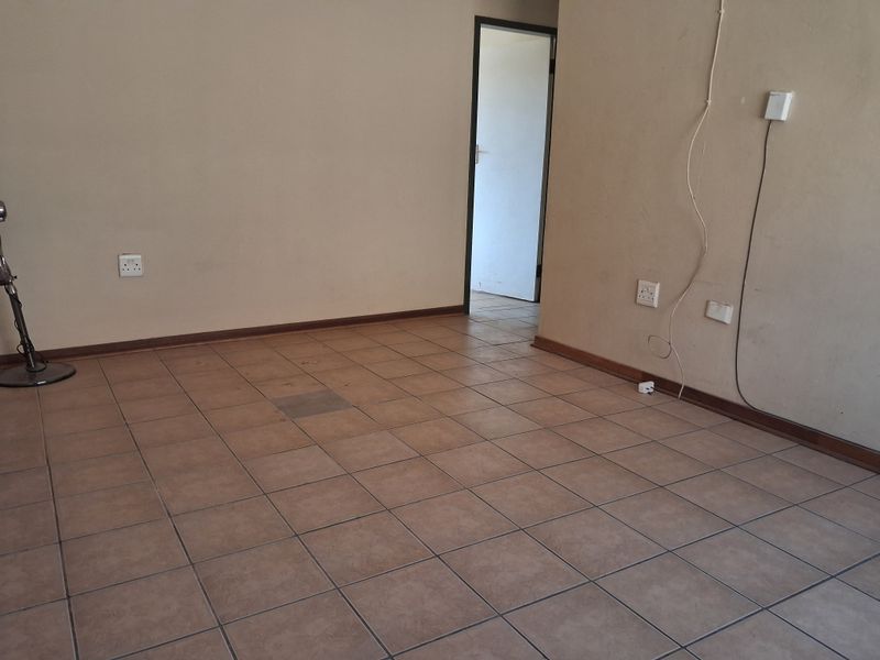 An empty living area featuring ceramic floor tiles, neutral wall paint, and standard electrical fixtures, ready for renovation or staging.