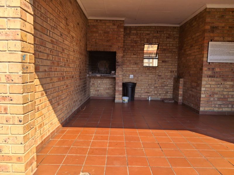 A covered patio area featuring facebrick walls, tiled flooring, and a built-in braai, offering a functional outdoor entertainment space.