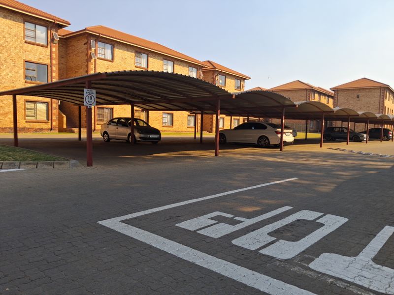 Exterior view of an apartment complex featuring a covered parking area with paved driveway and brick building facade.