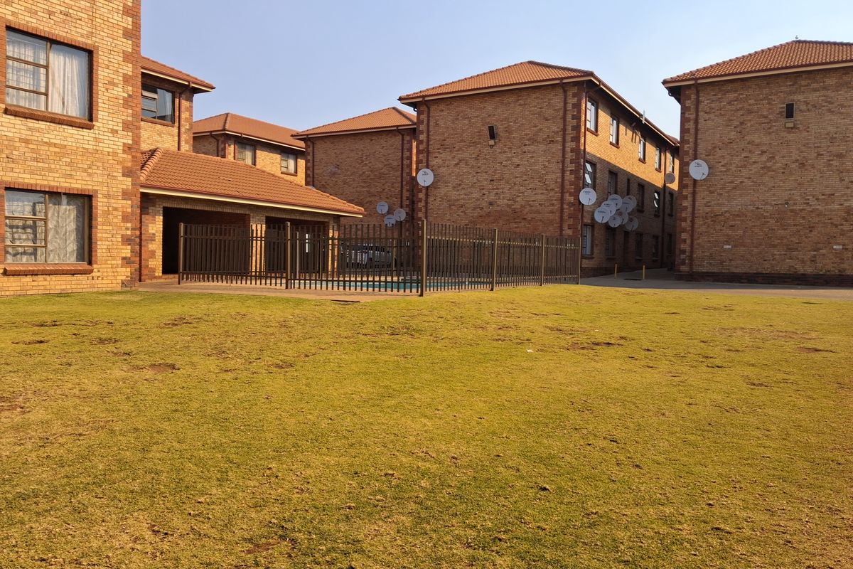 Exterior view of the apartment complex featuring face brick buildings, a communal swimming pool area, and a shared lawn.
