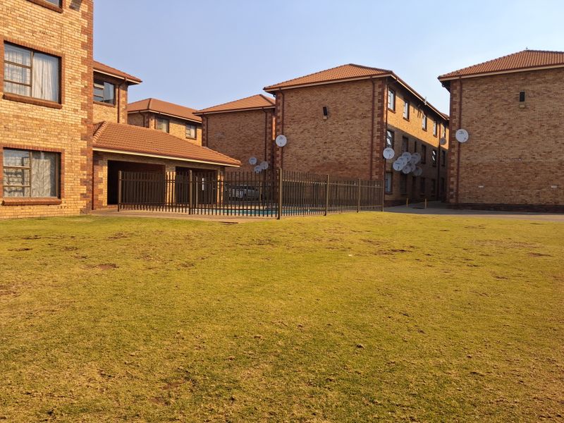 Exterior view of the apartment complex featuring face brick buildings, a communal swimming pool area, and a shared lawn.