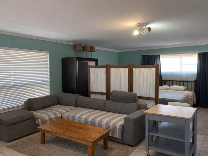 An open-plan living and sleeping area featuring tiled flooring, neutral wall tones, and functional window treatments.