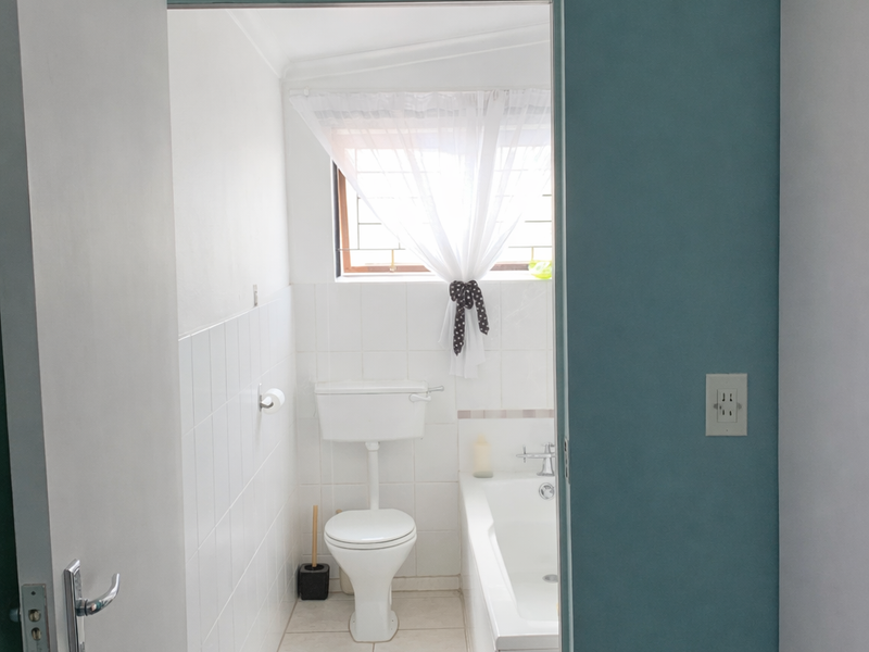 A functional bathroom featuring a standard bathtub, toilet, and tiled finishes, viewed through an open doorway.