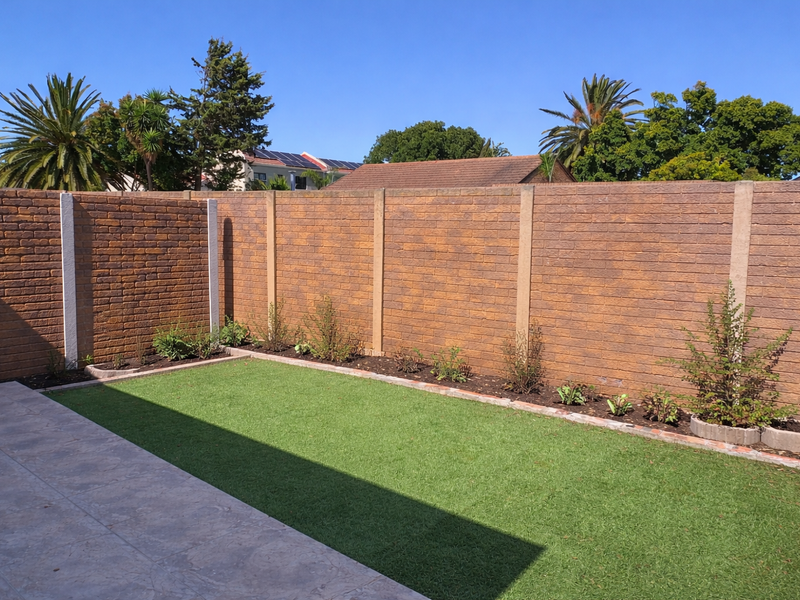 A well-maintained private garden featuring a neat artificial lawn, paved patio area, and secure brick boundary walls.