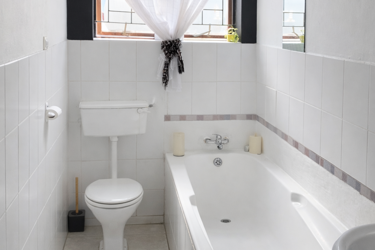 A functional bathroom featuring a white bathtub, pedestal basin, and toilet with classic white wall and floor tiling.