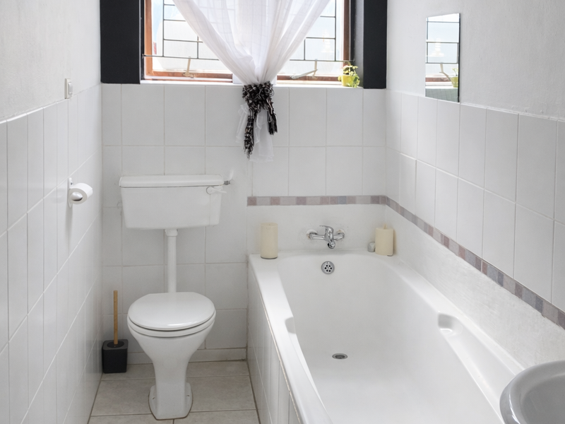 A functional bathroom featuring a white bathtub, pedestal basin, and toilet with classic white wall and floor tiling.