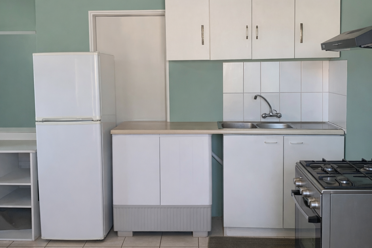A functional kitchen featuring white cabinetry, a stainless steel sink with tiled splashback, and a gas stove with an extractor fan.