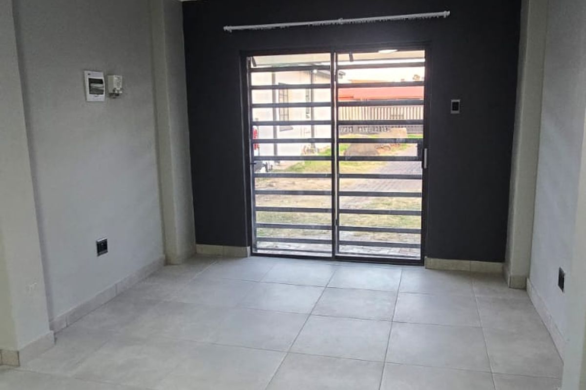 A bright, empty living area featuring neutral tiled flooring, modern grey accent walls, and a sliding glass door with an integrated security gate.