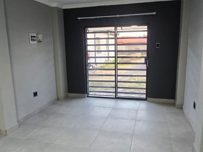 A bright, empty living area featuring neutral tiled flooring, modern grey accent walls, and a sliding glass door with an integrated security gate.