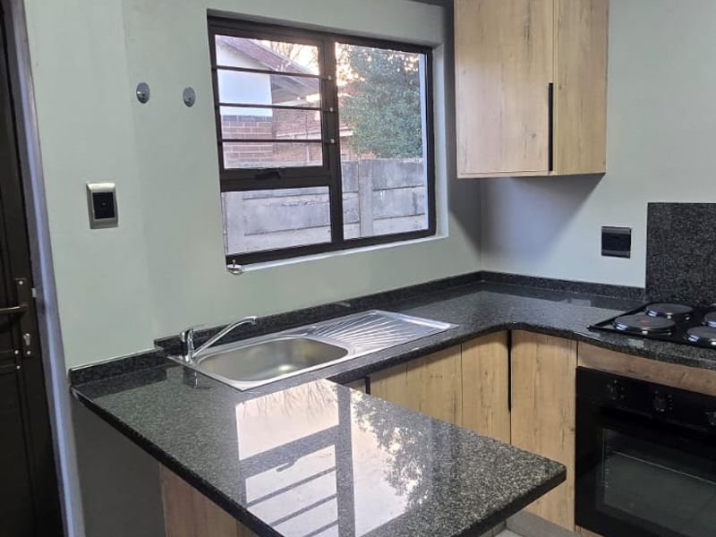 Modern kitchen featuring granite countertops, built-in oven, gas hob, and light wood-finish cabinetry with tiled flooring.