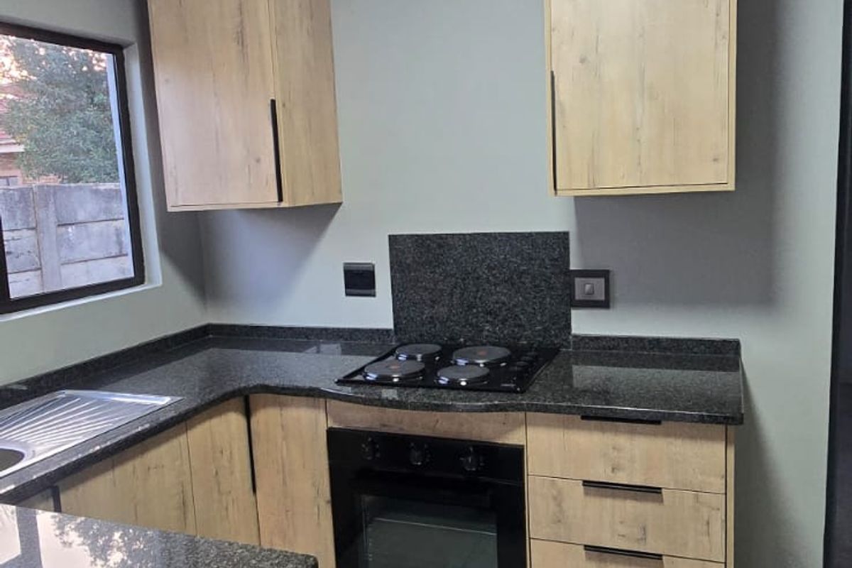 Modern kitchen featuring light wood-finish cabinetry, dark granite countertops, a built-in oven, electric hob, and neutral tiled flooring.