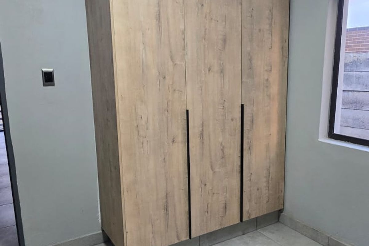A clean, empty bedroom featuring modern wood-look built-in cupboards, neutral grey tiled flooring, and crisp white cornicing.