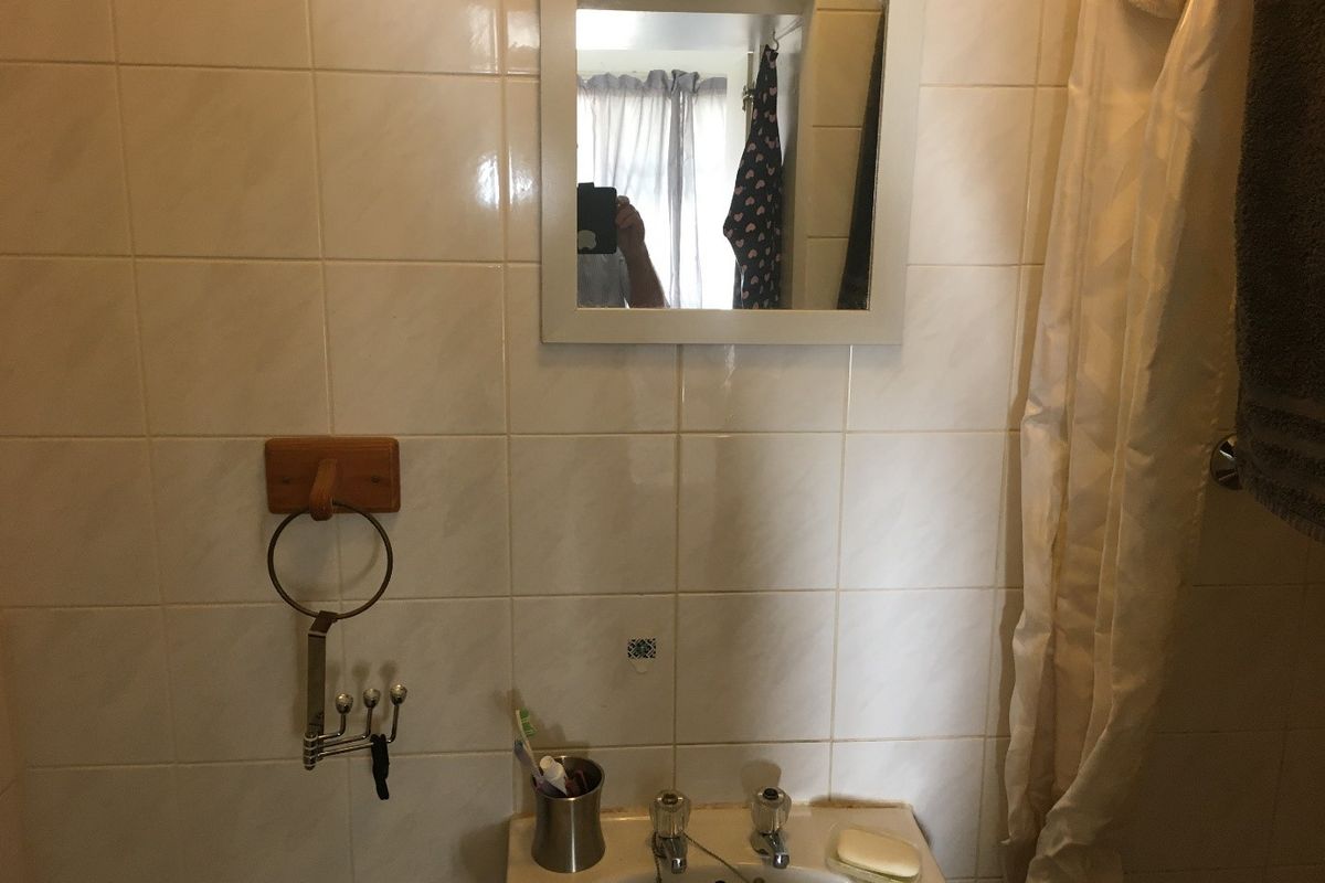 A dated bathroom featuring tiled walls, a pedestal basin with dual-handle taps, and a wall-mounted mirror.